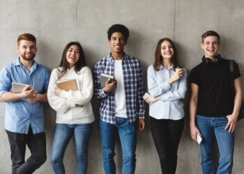 College students with books smiling to camera over grey wall, having break