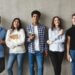 College students with books smiling to camera over grey wall, having break